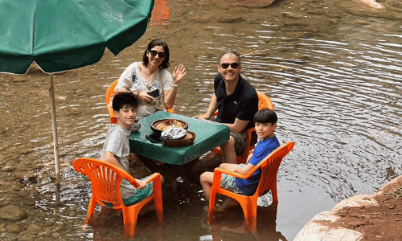 Family sitting in the natural rock pools of Paradise Valley Morocco eating traditional Moroccan tagine — family day trip from Taghazout to the Atlas Mountain foothills