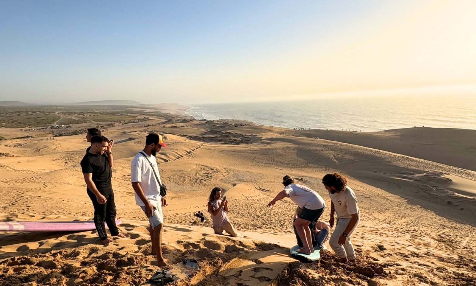 Small group sandboarding safely at Timlalin Dunes near Taghazout at sunset